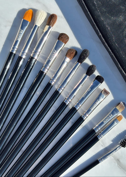Set of makeup brushes with black handles and silver ferrules on a light gray surface, with a black brush case in the background.